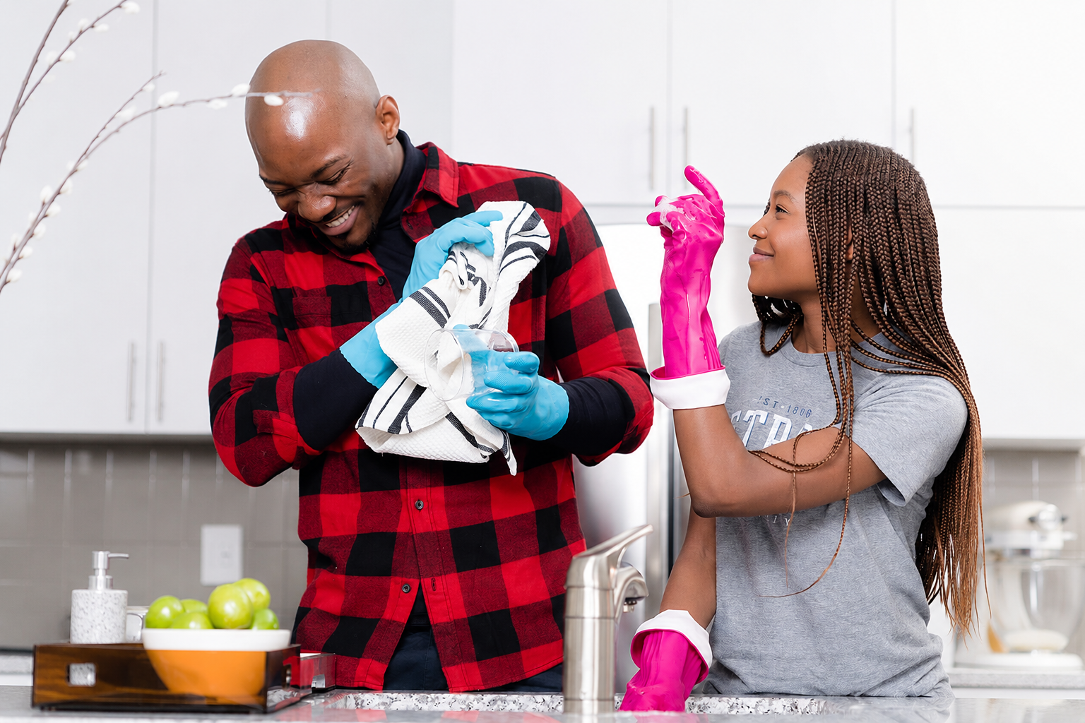 Two people wearing waterproof cleaning gloves while washing dishes to help protect the skin around the nails and reduce the risk of chronic paronychia.